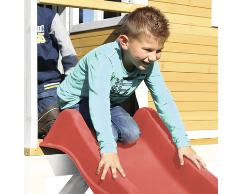 Junge rutscht auf einer roten Kinderrutsche an einem Spielhaus.