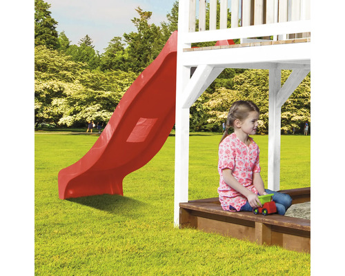 Kind sitzt im Sandkasten unter einem Spielturm mit Rutsche.