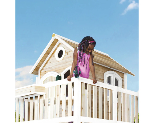 Mädchen auf einem Holzspielhaus mit Aussichtsplattform unter blauem Himmel
