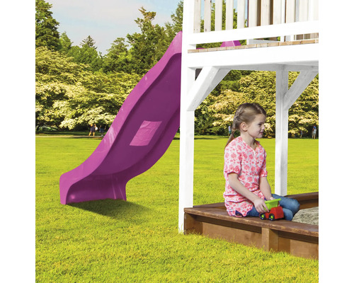 Mädchen sitzt im Sandkasten unter einem Spielhaus mit Rutsche