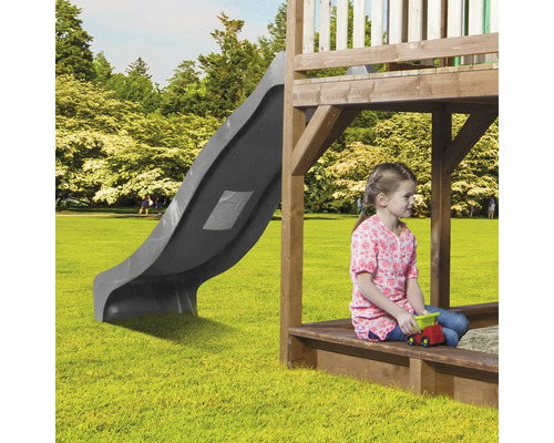 Kind sitzt im Sandkasten eines Spielhauses mit Rutsche im Garten.