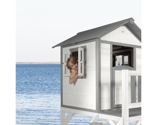 Maisonnette en bois sur pilotis avec enfant à la fenêtre devant un paysage marin