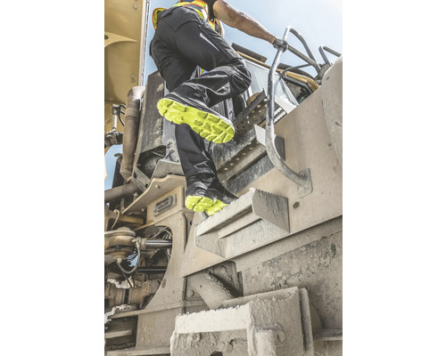 Ein Mann steigt mit Arbeitsschuhen auf eine Baumaschine.