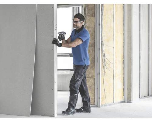 Un homme fixe une plaque de plâtre avec une visseuse sans fil sur une construction murale.