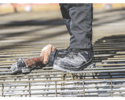 Personne portant des chaussures de sécurité Uvex et une cisaille à béton sans fil sur un chantier