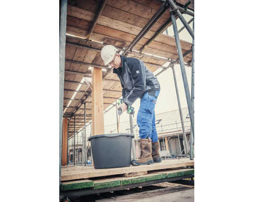 Handwerker mischt Mörtel mit einem elektrischen Rührer auf einem Gerüst.