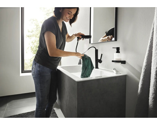 Frau wäscht ein Tuch in einem Waschbecken mit schwarzer Armatur und Handbrause in einem modernen Badezimmer