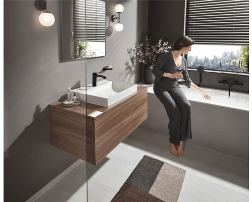 Salle de bain lumineuse avec lavabo, miroir, éclairage et baignoire avec femme