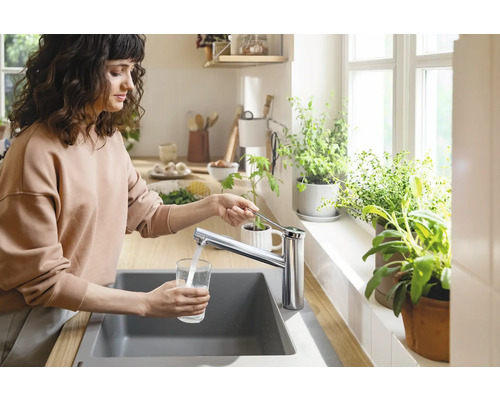 Frau füllt Wasser in ein Glas am Spültisch mit Armatur in einer hellen Küche.