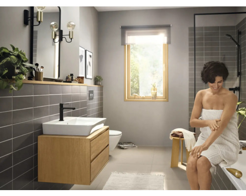 Helles Badezimmer mit Waschbeckenunterschrank, Spiegel, Dusche und einer Frau, die sich eincremt