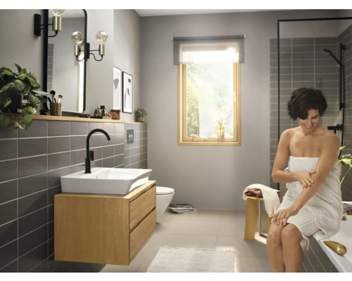 Salle de bains lumineuse avec lavabo, miroir, douche et une femme avec une serviette