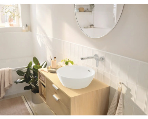 Salle de bains lumineuse avec vasque à poser, meuble-lavabo et robinetterie murale devant un dosseret de carrelage blanc