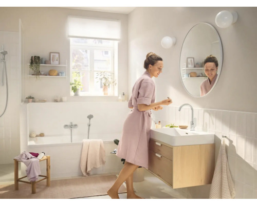 Salle de bain lumineuse avec baignoire, meuble sous-lavabo et femme devant le miroir
