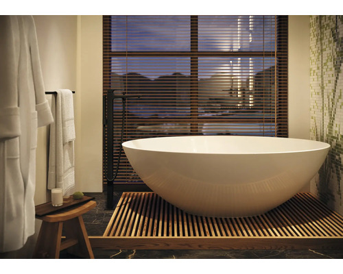 Freistehende Badewanne mit Armatur und Badaccessoires in hellem Badezimmer.