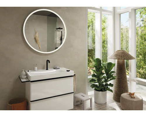 Modernes Badezimmer mit Waschtisch, rundem Spiegel mit Beleuchtung und großem Fenster.