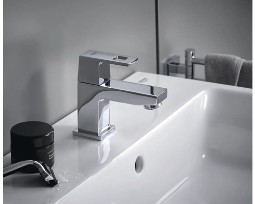 Sur un lavabo, on peut voir un robinet Grohe brillant avec un bec carré.