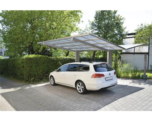 Une voiture blanche est garée sous un abri de voiture sur une aire de stationnement pavée.