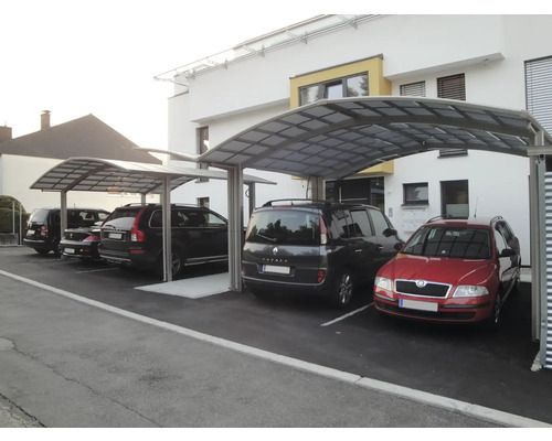 Plusieurs voitures garées sous un abri de voiture devant un bâtiment.