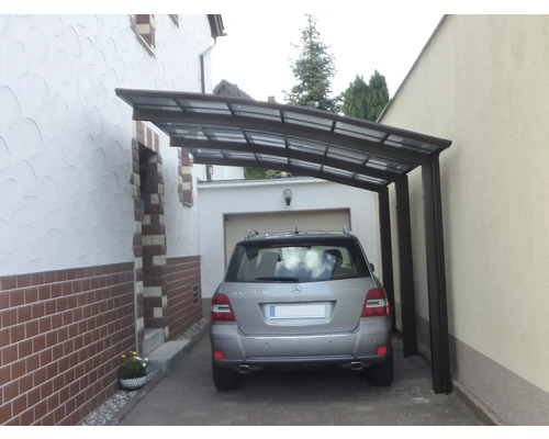 Une voiture est garée sous un carport entre deux bâtiments.
