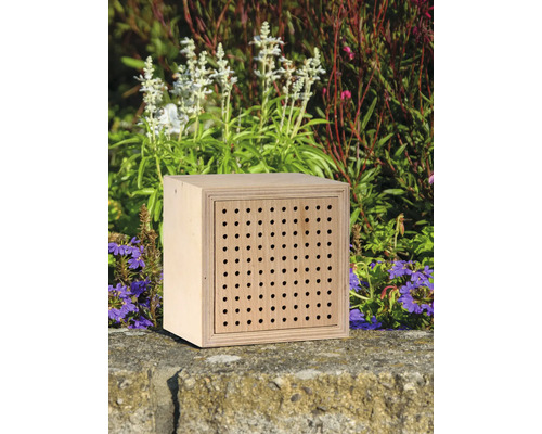 Insektenhotel aus Holz mit vielen Löchern vor Blumen