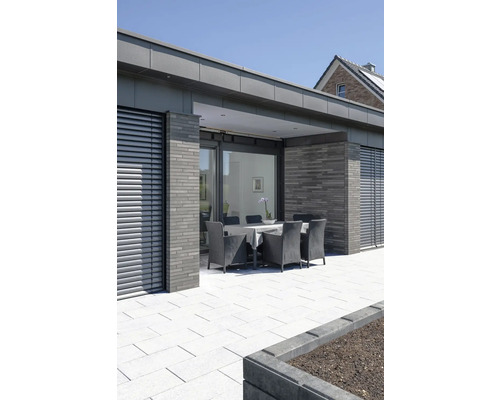 Terrasse mit Gartenmöbeln, Steinboden und modernem Haus im Hintergrund