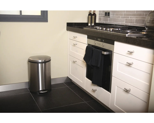 Scène de cuisine avec poubelle à pédale en acier inoxydable, four et armoires de cuisine blanches