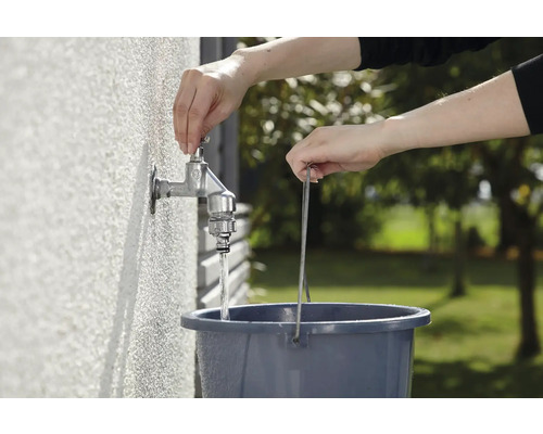 Eine Person füllt Wasser aus einem Wasserhahn in einen Eimer.