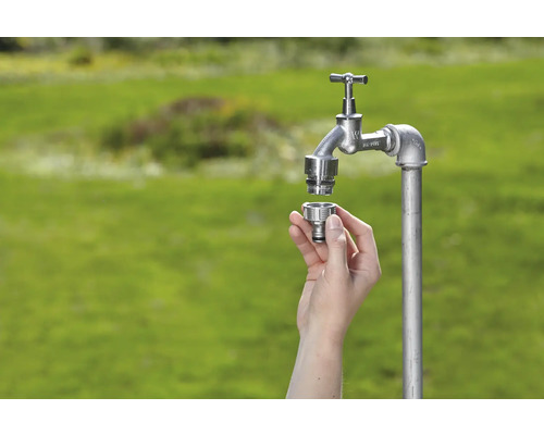 Aussenwasserhahn mit Schnellkupplung in der Hand vor grünem Hintergrund