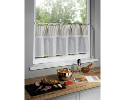 Küchenszene mit Bistrogardine, Salatschüssel, Brot, Gemüse und Kochbuch auf einer Küchentheke vor einem Fenster.