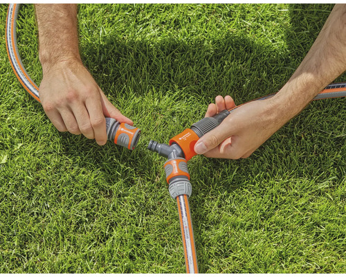 Deux mains raccordent un tuyau d''arrosage à un raccord en Y sur une pelouse.