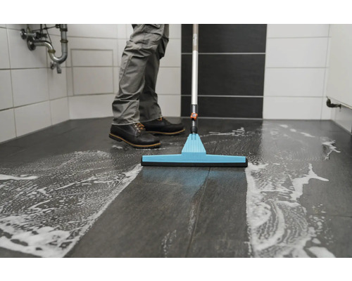 Agent de nettoyage essuyant le sol de la salle de bain avec du détergent et une raclette