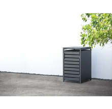 Mülltonnenbox mit Lamellenfront vor einer weißen Wand und unter einem Baum