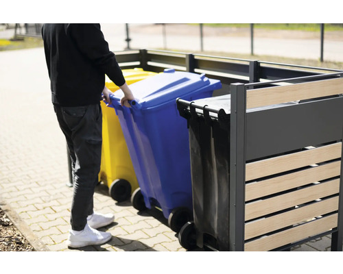 Person schiebt blaue Mülltonne in eine Mülltonnenbox
