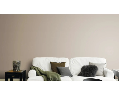 Salon avec canapé blanc, coussins, couverture et vase décorative sur une table d''appoint devant un mur uni