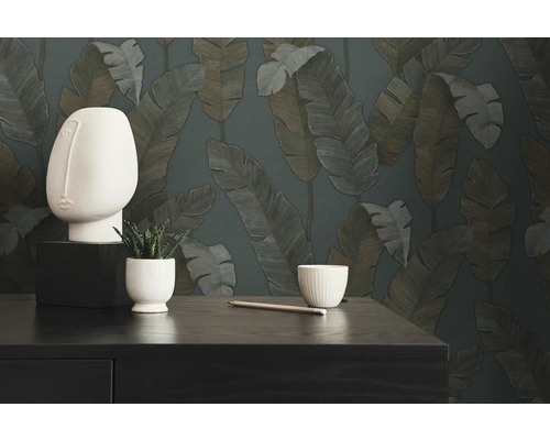 Dekorative Szene mit einer abstrakten Kopfskulptur, einer Topfpflanze, einem Stift und einer Schale vor einer Tapete mit Blattmuster