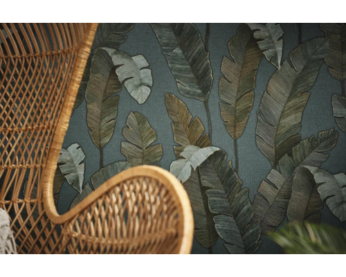 Nahaufnahme eines Korbsessels vor einer Tapete mit Blattmuster.