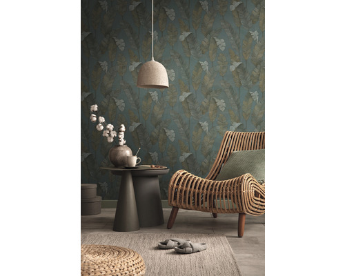 Wohnzimmer mit Blattmuster-Tapete, Rattansessel, Beistelltisch und Textillampe für eine wohnliche Atmosphäre