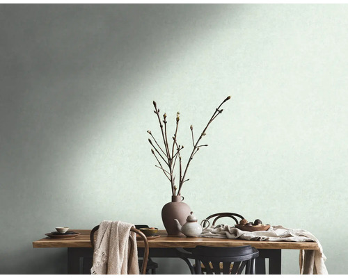 Einladende Szene mit einem gedeckten Holztisch, Geschirr, einer Vase mit Zweigen und einer hellen Wand im Hintergrund