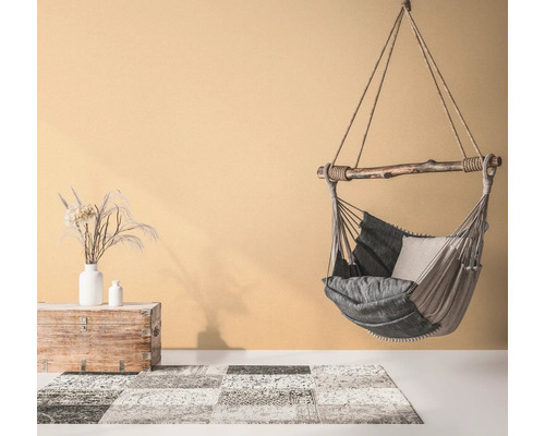 Hängesessel mit Kissen, Teppich mit Muster und Holztruhe mit Vasen in einem hellen Raum.