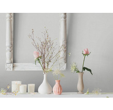Wohnraum-Szene mit floralen Dekorationen, Kerzen und einem Bilderrahmen vor einer gemusterten Tapete