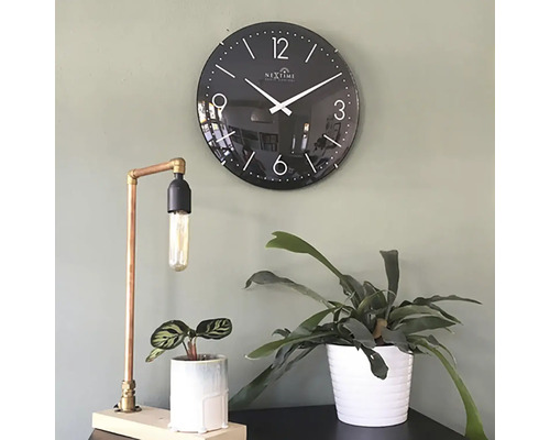 Dekorative Szene mit einer schwarzen Wanduhr, einer Tischlampe aus Kupfer und zwei Zimmerpflanzen in Töpfen.