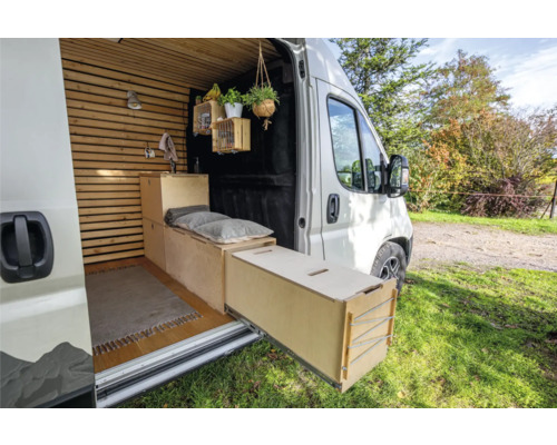 Innenraum eines umgebauten Lieferwagens mit Holzauskleidung, Möbeln und Ausziehfach