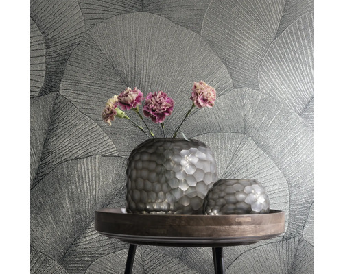 Zwei Vasen und Blumen auf einem Tisch vor einer Wand mit Blattmuster-Tapete.