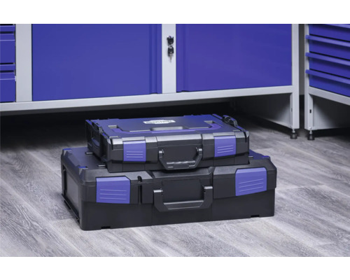 Zwei Werkzeugkoffer unterschiedlicher Größe, gestapelt vor einem Werkstattschrank.