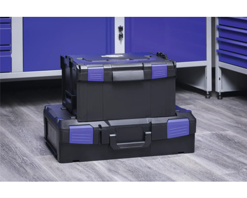 Deux boîtes à outils noires avec fermetures bleues empilées devant une armoire d''atelier bleue.