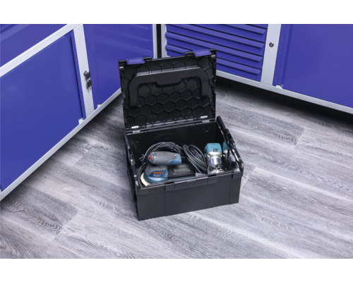 Boîte à outils ouverte avec outils électriques devant des armoires métalliques bleues