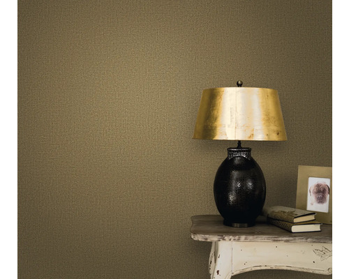 Nahaufnahme einer Wand mit einer Textiltapete, einem Nachttisch, einer Lampe, einem Bilderrahmen und Büchern.