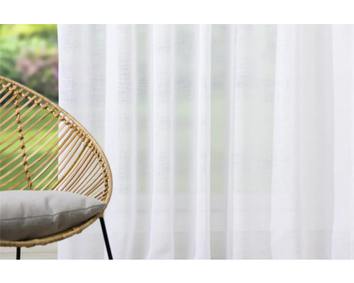 Pièce lumineuse avec rideau blanc et fauteuil en rotin