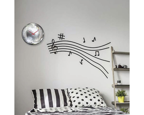 Wanddekoration mit Spiegelkugel-Uhr und Notenlinien-Wandaufkleber über einem Bett.