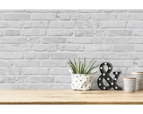 Aménagement décoratif d''une pièce avec papier peint en briques, plante, symbole ''&'' et récipients sur une table en bois.